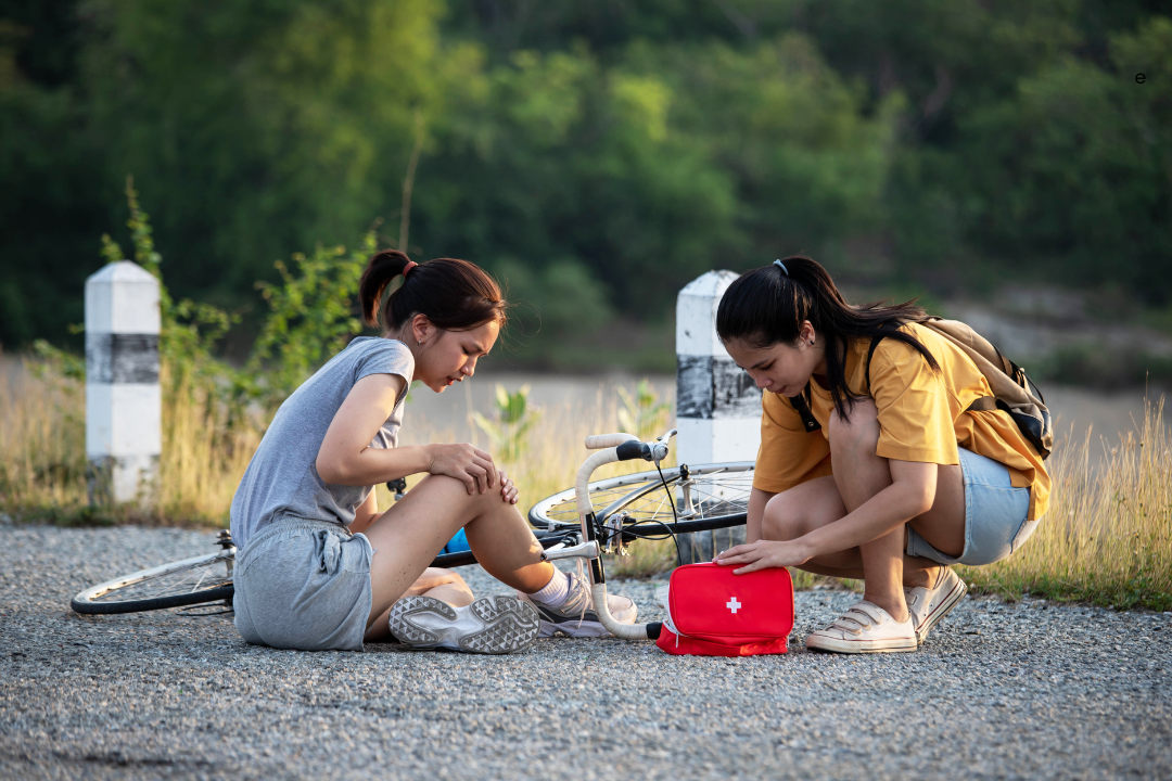 two women sitting on the ground with a bicycle and first aid kit